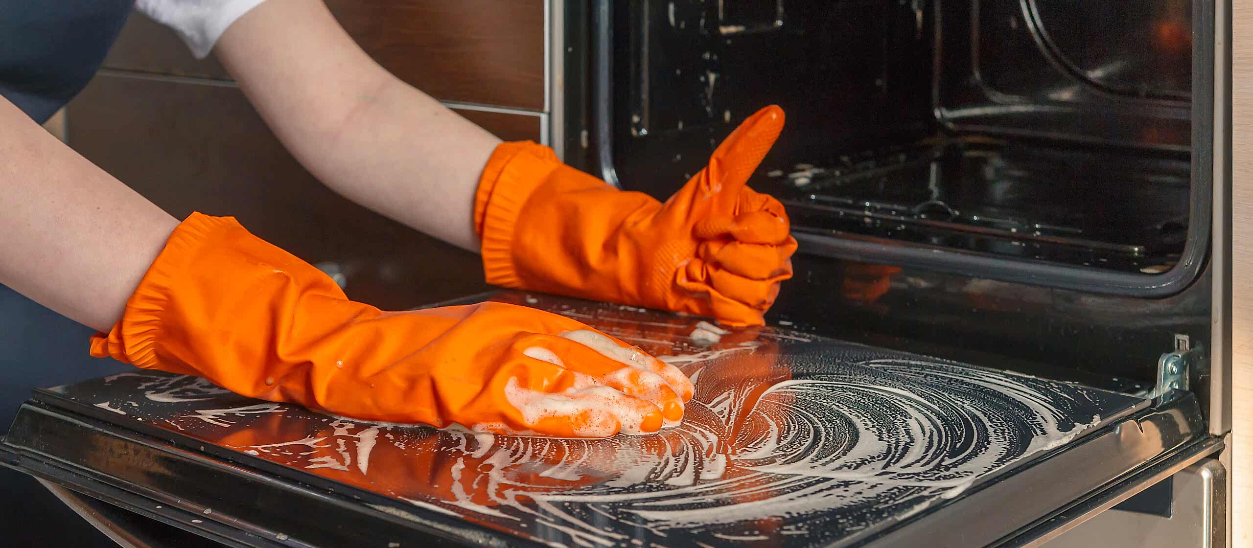 Kitchen cleaning. Girl's hands in gloves wash clean the stove, kitchen oven in the kitchen.